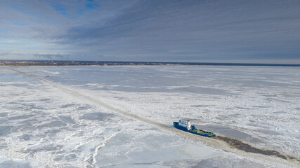 aerial view to the ice breaker assisting cargo ship to reach the harbor via waterway through the fro