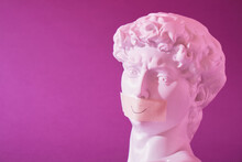 Copy Of The Head Of An Antique Statue Of David With A Taped Mouth In Pink Neon Light On A Purple Background