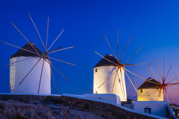 Wall Mural - Mykonos, Greece. Traditional windmills. The symbol of Mykonos during  sunset. Landscape during sunset. Sea shore and beach. Photo for travel and vacation.