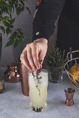 Wall Mural - Real woman preparing Pear Collins Cocktail in highball glass on light gray table surface surrounded by ingredients and bar tools