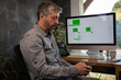 © Tof - Photographie - homme de 50 ans en télétravail dans son bureau devant son ordinateur. il consulte son téléphone portable. Employé de bureau qui travaille chez lui