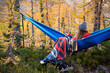 © Cavan Images - Female relaxing in a hammock in a forest of larches in the fall