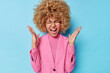 © wayhome.studio  - Indoor shot of emotional young woman keeps palms raised exclaims loudly reacts on amazing news dressed formally wears round spectacles isolated over blue background. Human emotions and feelings