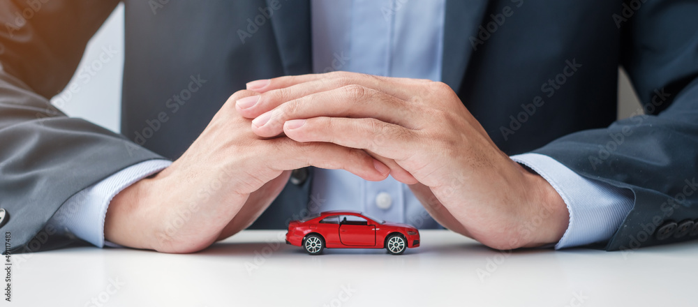 Businessman hand cover or protection red car toy on table. Car insurance, warranty, repair, Financial, banking and money concept