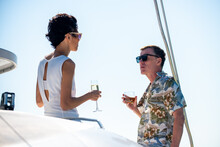 Caucasian Couple Enjoy Outdoor Luxury Party Drinking Champagne With Talking Together While Catamaran Boat Sailing At Sunset. Man And Woman Relax With Outdoor Lifestyle On Summer Travel Vacation