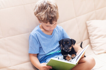 A boy with a little dog is reading a book