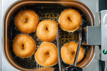 Donuts frying in deep fat. Preparation of traditional donuts, six round donuts in boiling oil.