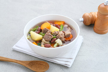 Wall Mural - Sup daging kacang merah, clear soup with beef slices, red bean and vegetables. Served in bowl on grey background. Selected focus.
