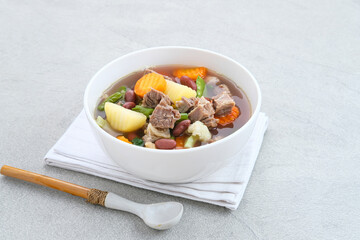 Wall Mural - Sup daging kacang merah, clear soup with beef slices, red bean and vegetables. Served in bowl on grey background. Selected focus.
