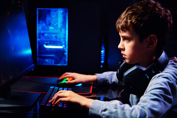 Teenager boy play computer video game in dark room, use neon colored rgb mechanical keyboard, workplace for cybersport gaming, children gaming addiction