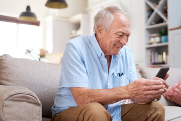 Would you look at that.... Shot of an elderly man looking happy while using his smartphone at home on the sofa.