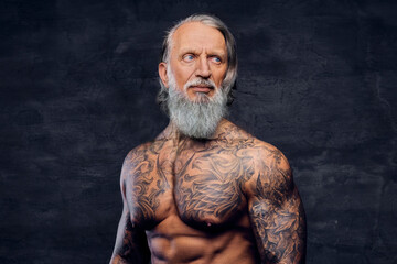 Muscular elderly man with tattooed body against dark background