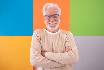 Wall Mural - Adult handsome senior man crossed arms looking at camera smiling over colorful cute background. Caucasian 70 years old white-haired bearded man posing for portrait wearing eyeglasses. Copy space