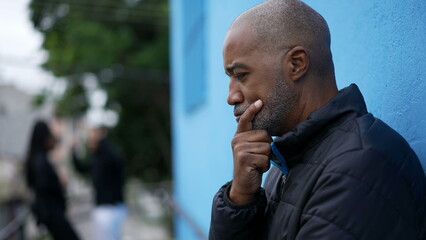 A pensive black senior man thinking about decision standing outside in street