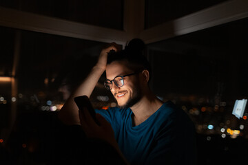 Dark portrait of smiling man using smartphone on background night city.