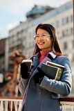 Fototapeta Pomosty - Portrait of a happy Asian girl holds books and takeaway coffee outside in cold weather.