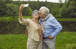 © Studio Romantic - Cheerful old wife making selfie by phone camera while tender loving husband sweet kissing her cheek. Retired people walking in city public park. Good memory and best vibes on pension concept