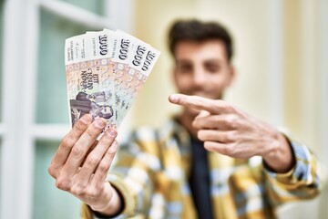 Handsome hispanic man smiling happy and confident at the city holding 1000 iceland krona banknotes