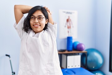 Wall Mural - Young latin woman wearing doctor uniform stretching arms at physiotherapy clinic