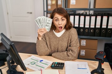 Poster - Young beautiful woman working at small business ecommerce holding money scared and amazed with open mouth for surprise, disbelief face