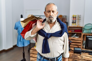 Poster - Handsome senior man holding shopping bags at boutique shop thinking attitude and sober expression looking self confident