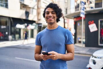 Sticker - Young hispanic man smiling confident using smartphone at street