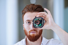 Young Man Looking Through Open Camera Lens At Office