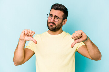 Young caucasian man isolated on blue background showing thumb down, disappointment concept.