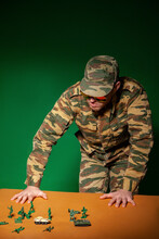 Young Military Soldier With Army Figurine Toys Standing By Table Against Green Background