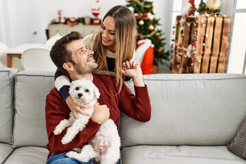 Canvas Print - Young hispanic couple smiling happy sitting on the sofa with dog at home.