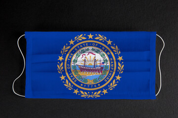 Wall Mural - Coronavirus Covid-19 in New Hampshire U.S. state. Flag of the State of New Hampshire printed on medical mask on black background. Coronavirus update in Manchester. State healthcare concept.	