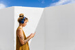 © Westend61 - Woman with headphones using smart phone in front of wall on sunny day