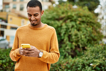 Wall Mural - Young african american man smiling happy using smartphone at the city.