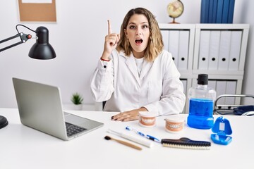 Wall Mural - Young hispanic woman working at dentist clinic pointing finger up with successful idea. exited and happy. number one.