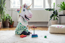 Girl In Unicorn Mask Playing With Toy Blocks At Home
