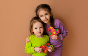 two cute sisters are holding puzzle hearts in their hands as a sign of support for children sufferin