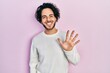 © Krakenimages.com - Handsome hispanic man wearing casual white sweater showing and pointing up with fingers number five while smiling confident and happy.