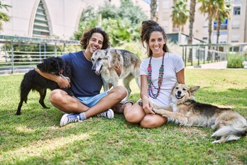 Wall Mural - Man and woman couple smiling confident sitting on herb with dogs at park