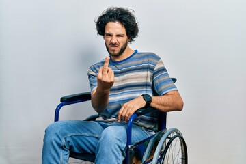 Canvas Print - Handsome hispanic man sitting on wheelchair showing middle finger, impolite and rude fuck off expression