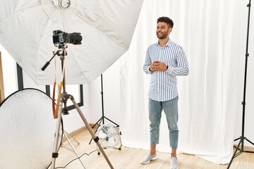 Canvas Print - Arab young man posing as model at photography studio hands together and fingers crossed smiling relaxed and cheerful. success and optimistic