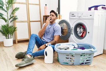 Wall Mural - Young hispanic man putting dirty laundry into washing machine bored yawning tired covering mouth with hand. restless and sleepiness.