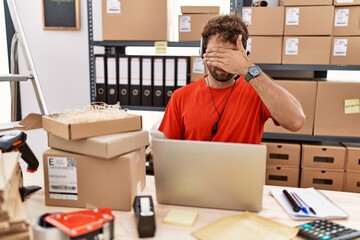 Poster - Young hispanic call center agent man working at warehouse covering eyes with hand, looking serious and sad. sightless, hiding and rejection concept