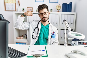 Poster - Young man with beard wearing doctor uniform and stethoscope at the clinic strong person showing arm muscle, confident and proud of power