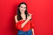 Young brunette woman wearing casual red shirt smiling cheerful pointing with hand and finger up to the side