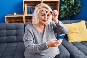 Middle age blonde woman using smartphone sitting on sofa at home