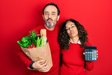 Sticker - Middle age couple of hispanic woman and man holding groceries bag and calculator looking at the camera blowing a kiss being lovely and sexy. love expression.