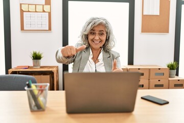 Poster - Middle age businesswoman sitting on desk working using laptop at office approving doing positive gesture with hand, thumbs up smiling and happy for success. winner gesture.