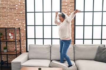 Poster - Middle age woman listening to music and dancing standing on sofa at home
