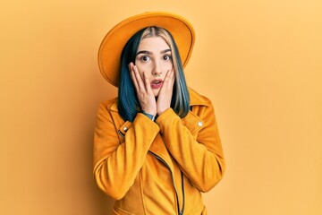 Wall Mural - Young modern girl wearing yellow hat and leather jacket afraid and shocked, surprise and amazed expression with hands on face