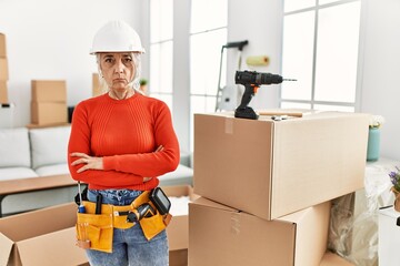 Poster - Middle age grey-haired woman wearing hardhat standing at new home skeptic and nervous, disapproving expression on face with crossed arms. negative person.